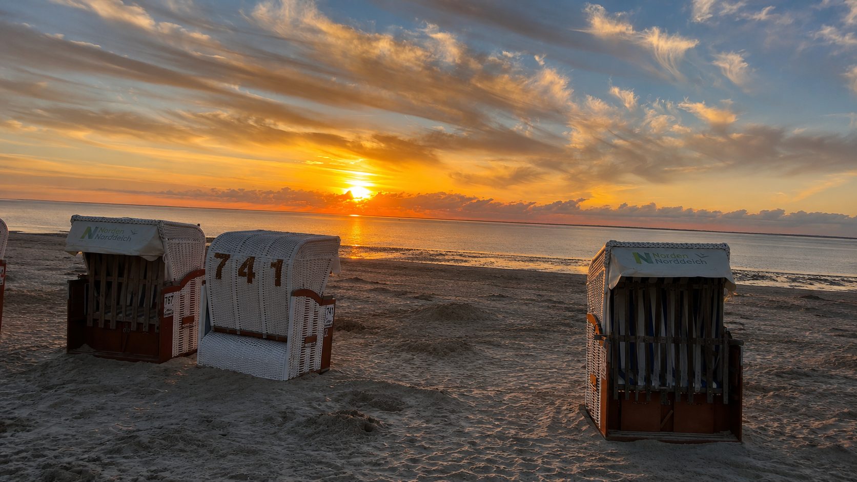 Sonnenuntergang am Norddeicher Strand mit Strandk&ouml;rben und Blick aufs Wattenmeer
